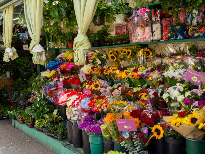 A vibrant flower shop display featuring a wide variety of fresh floral arrangements and bouquets. Bright sunflowers with large yellow petals and dark centers are prominently arranged, complemented by